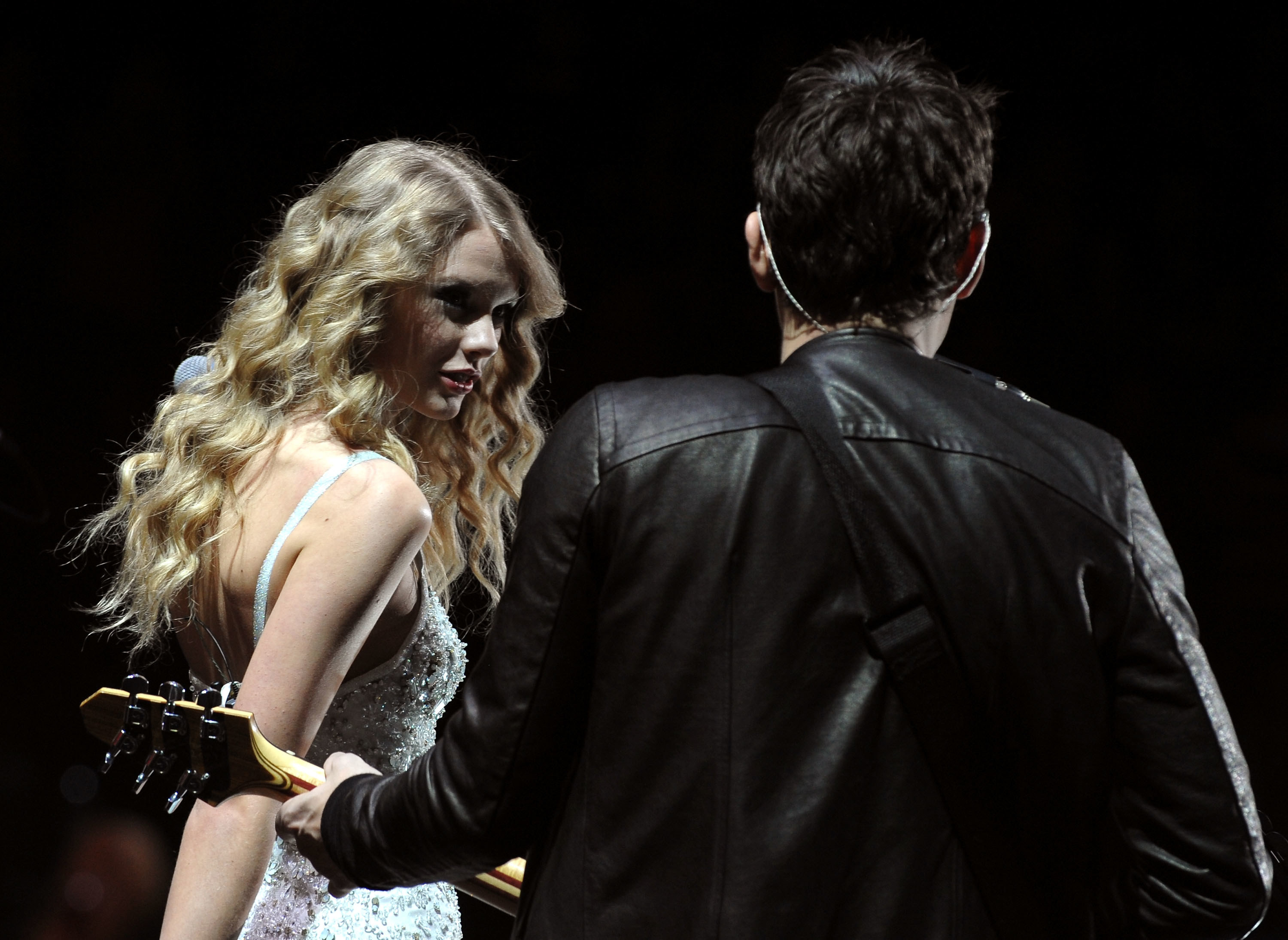 Taylor looks at John as he plays the guitar on stage