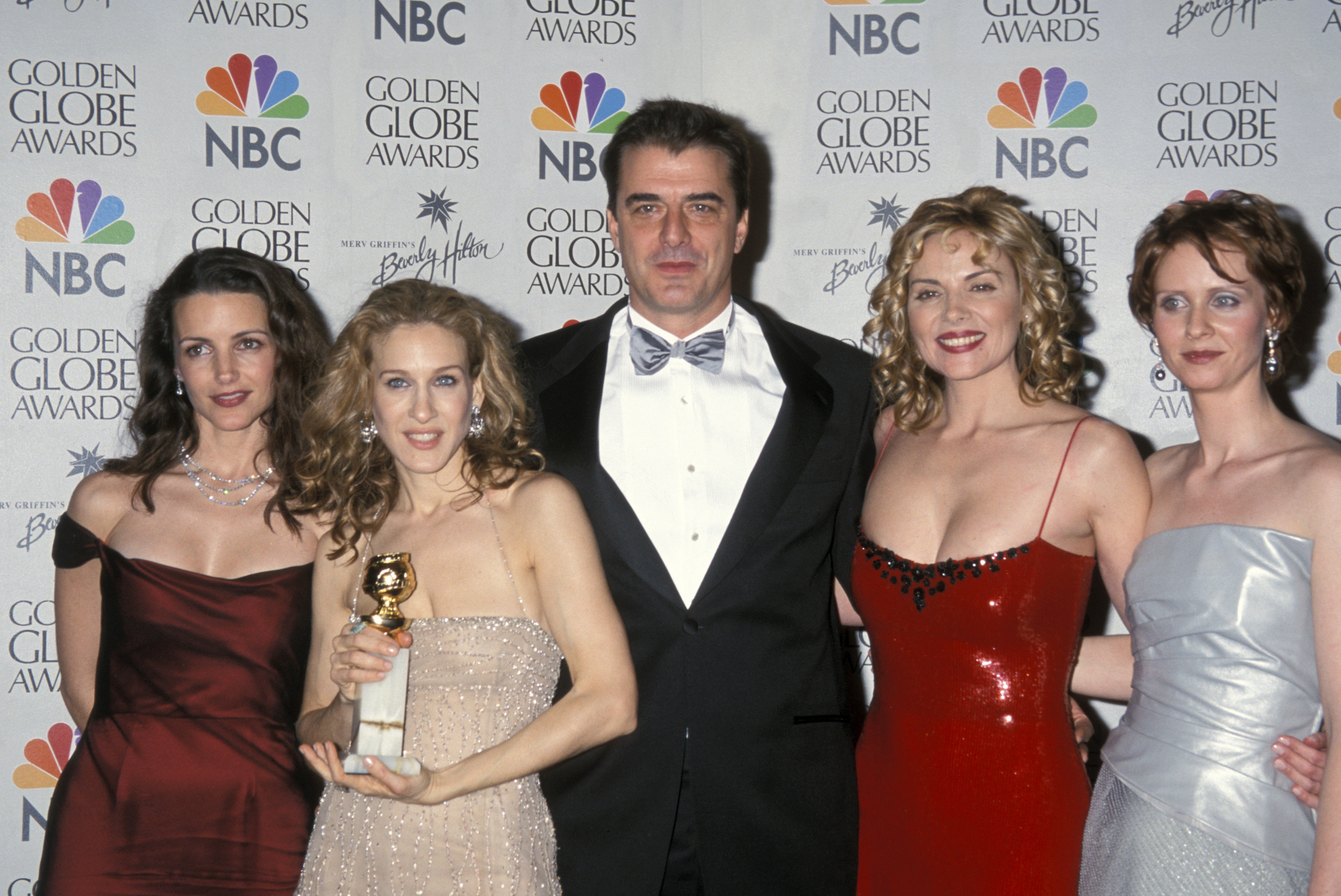 Kristin, SJP, Chris, Kim, and Cynthia standing together arm in arm with a Golden Globe award