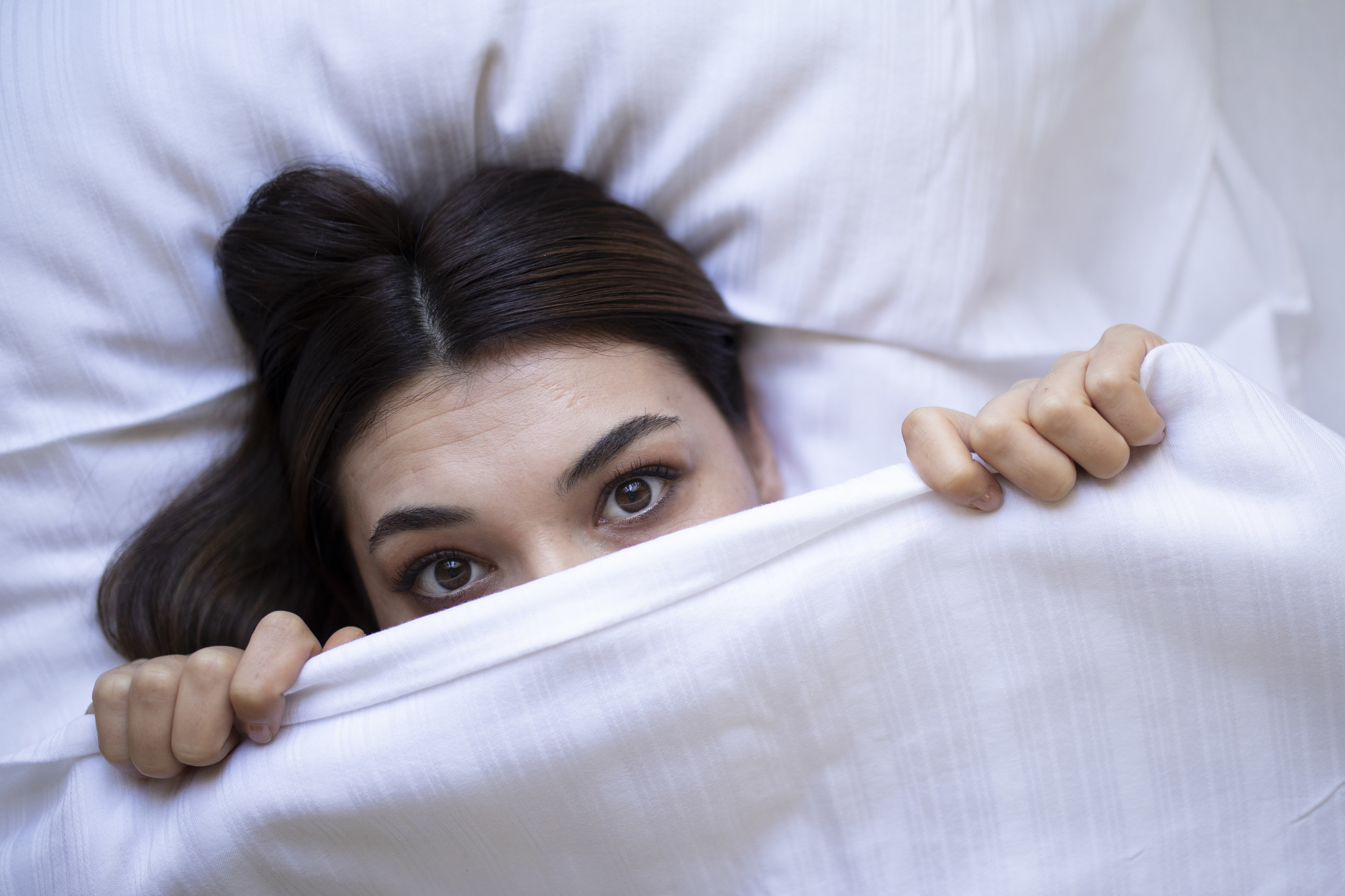 A woman holding a blanket over the bottom half of her face as she lays in bed