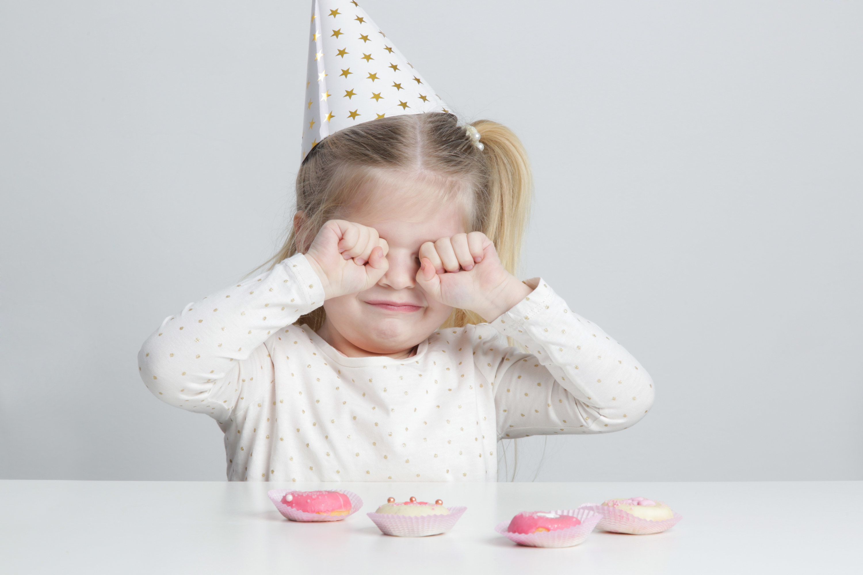 Displeased little girl with birthday hat and donuts in front of her