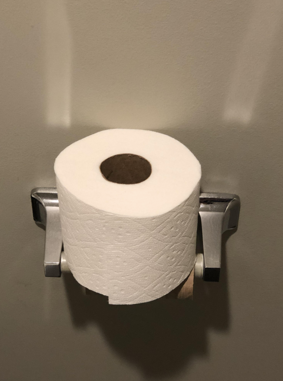 The new roll of toilet paper has been set on top of the holder instead of actually placed in it