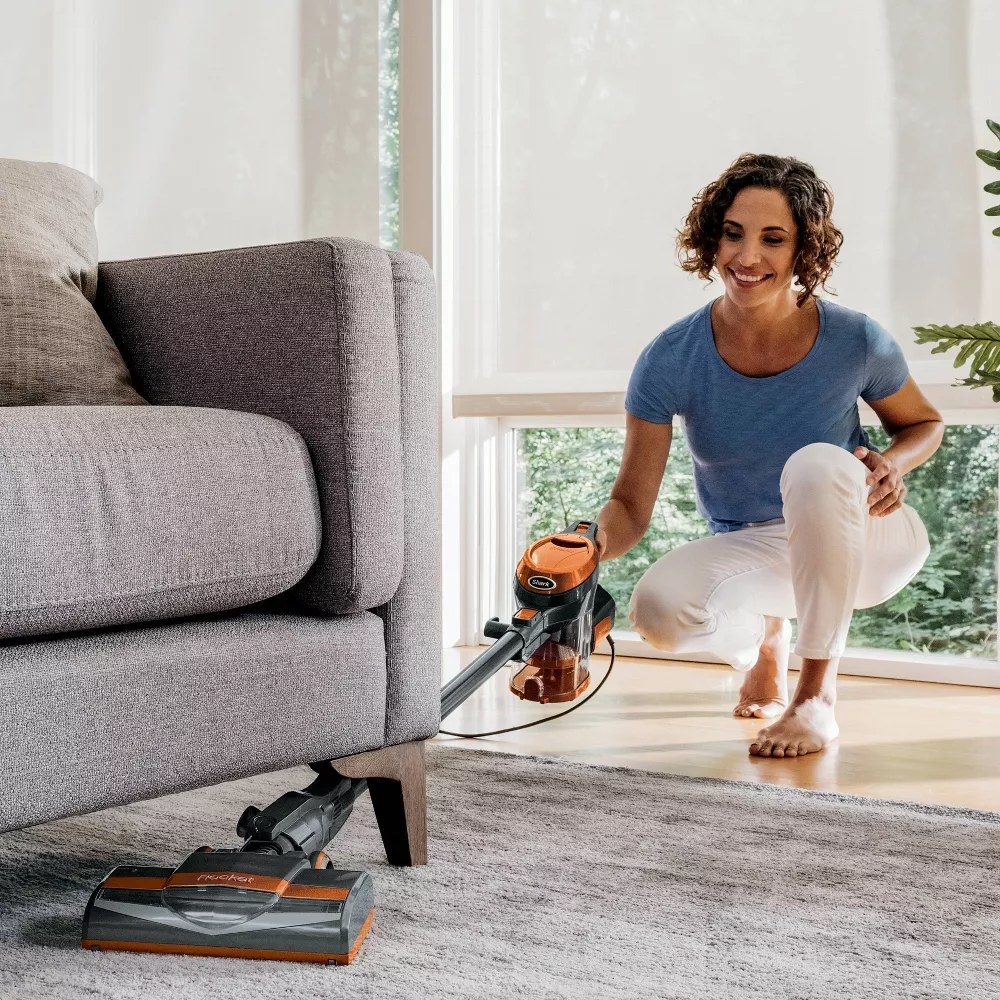 A model using the vacuum to clean under a couch