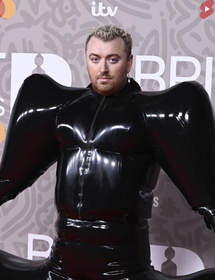A closeup of Sam Smith on the red carpet in a shiny, voluminous outfit