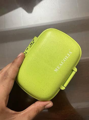 Reviewer's photo of a hand holding a green pill organizer.