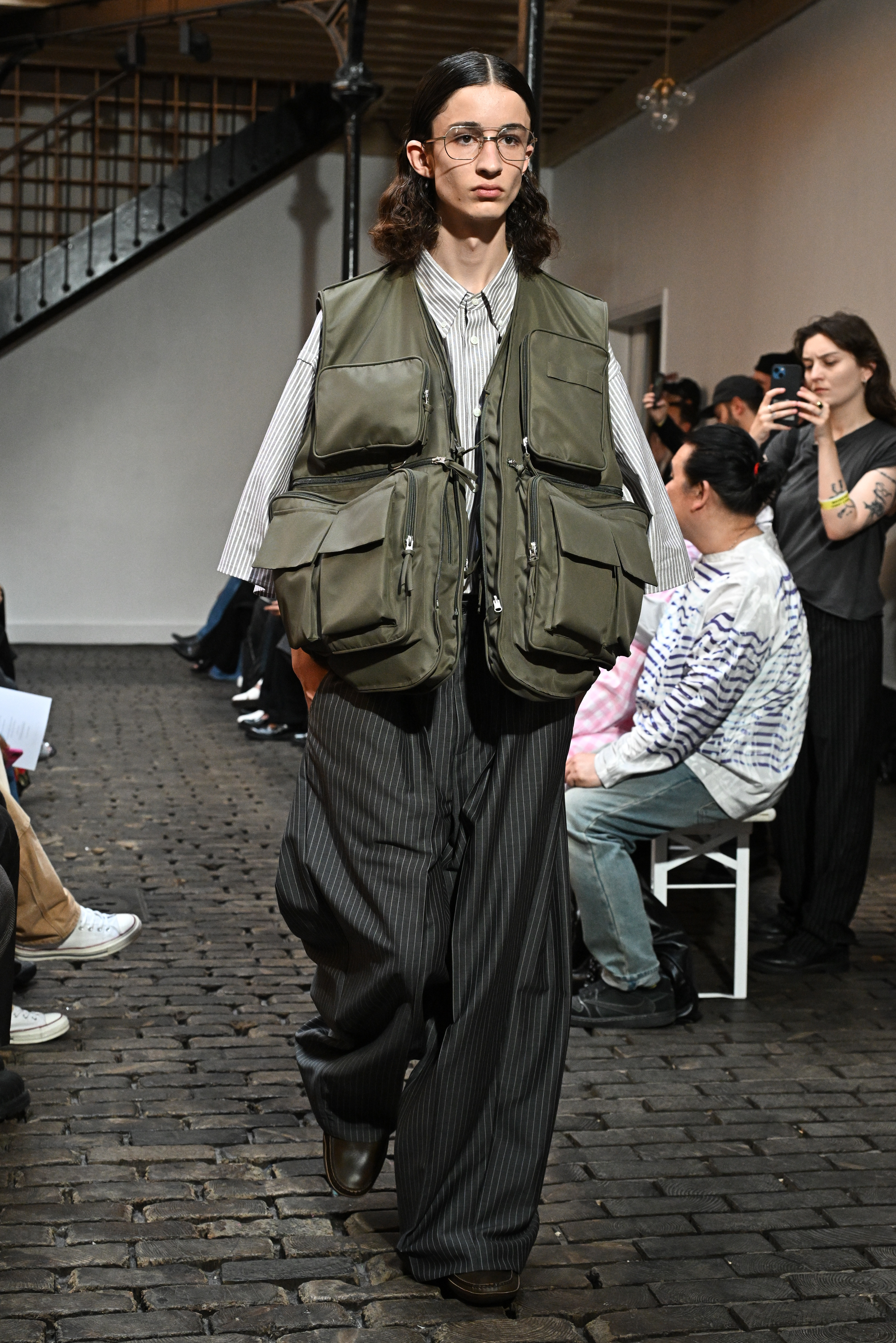 A model walks the runway during the Hed Mayner Menswear Spring/Summer 2024 show in an oversized fishing vest with slacks.