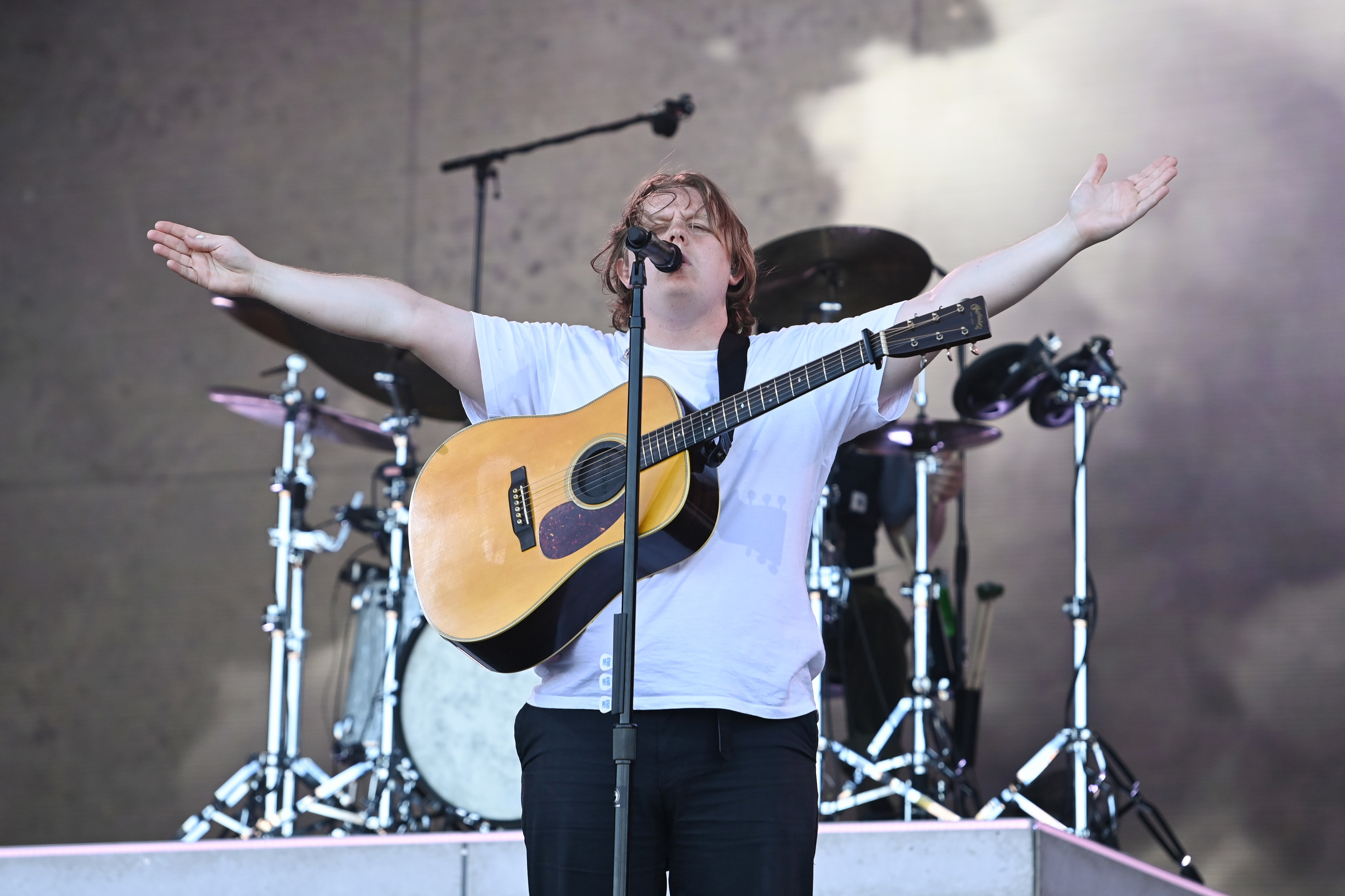 Lewis singing with his arms outstretched as his guitar is around his shoulder