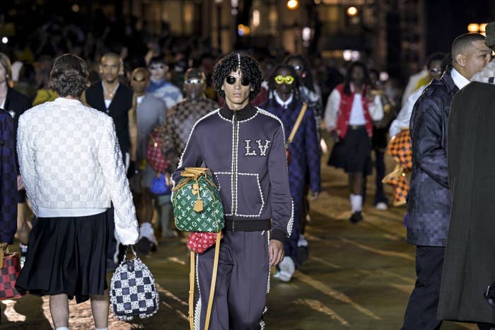 A model wears a Louis Vuitton tracksuit decorated with pearls and carries colorful leather duffle bags with Louis Vuitton&#x27;s monogram.