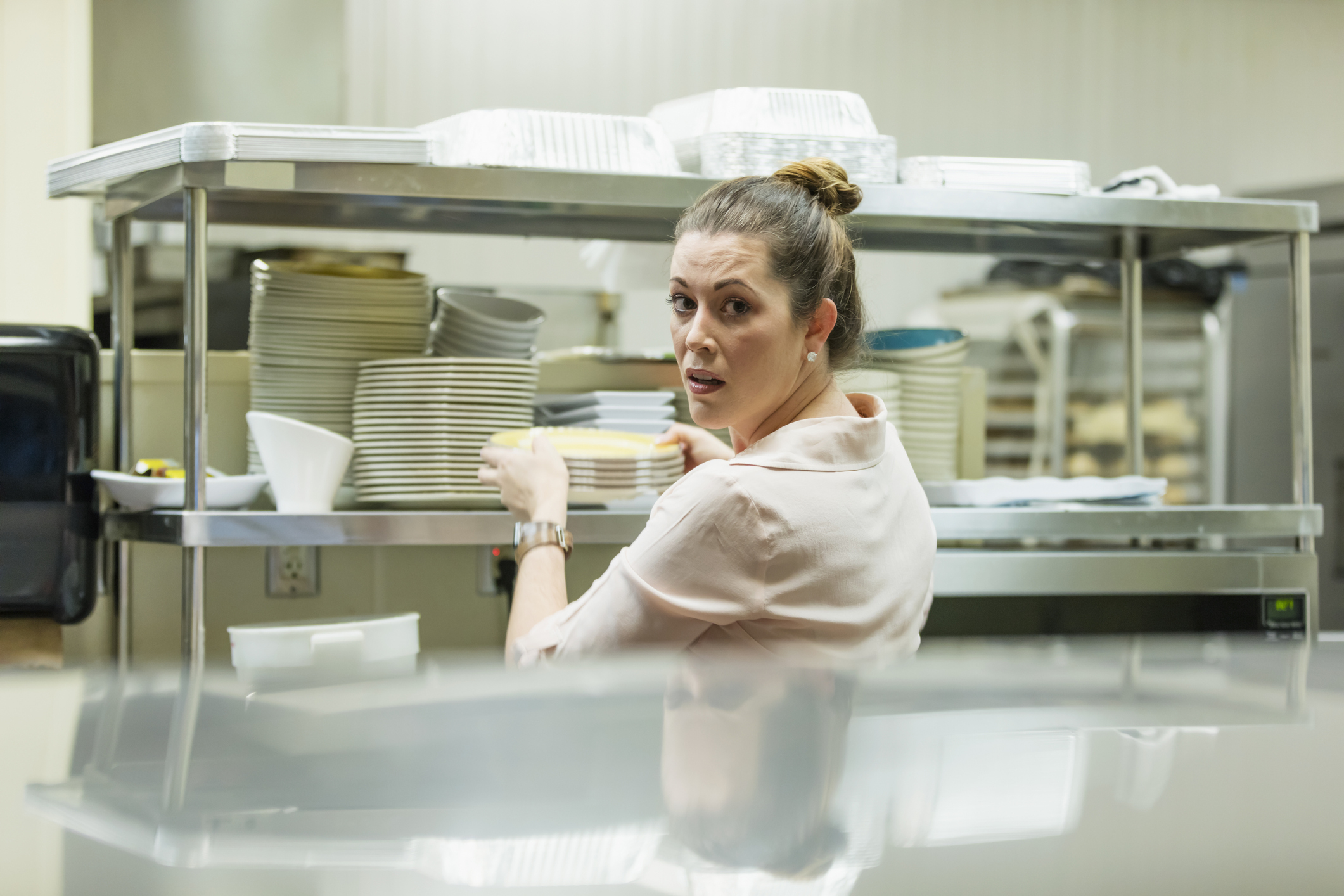 A woman in a restaurant kitchen grabbing plates