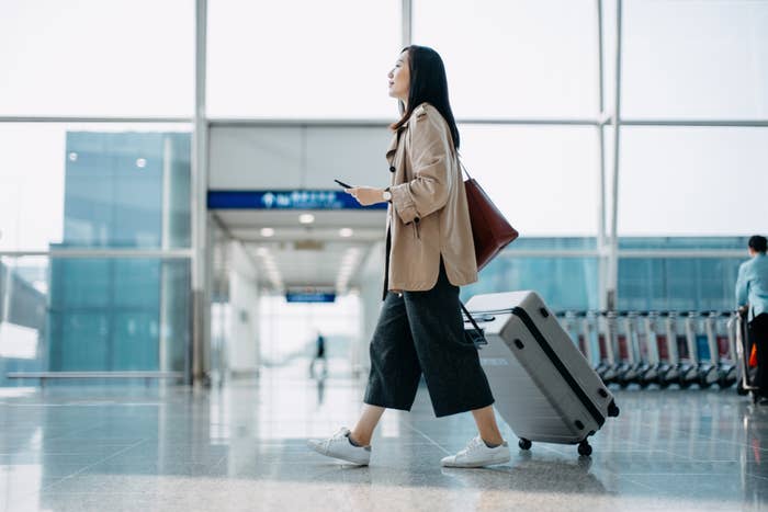 An Asian woman walking with a carry-on through an airport