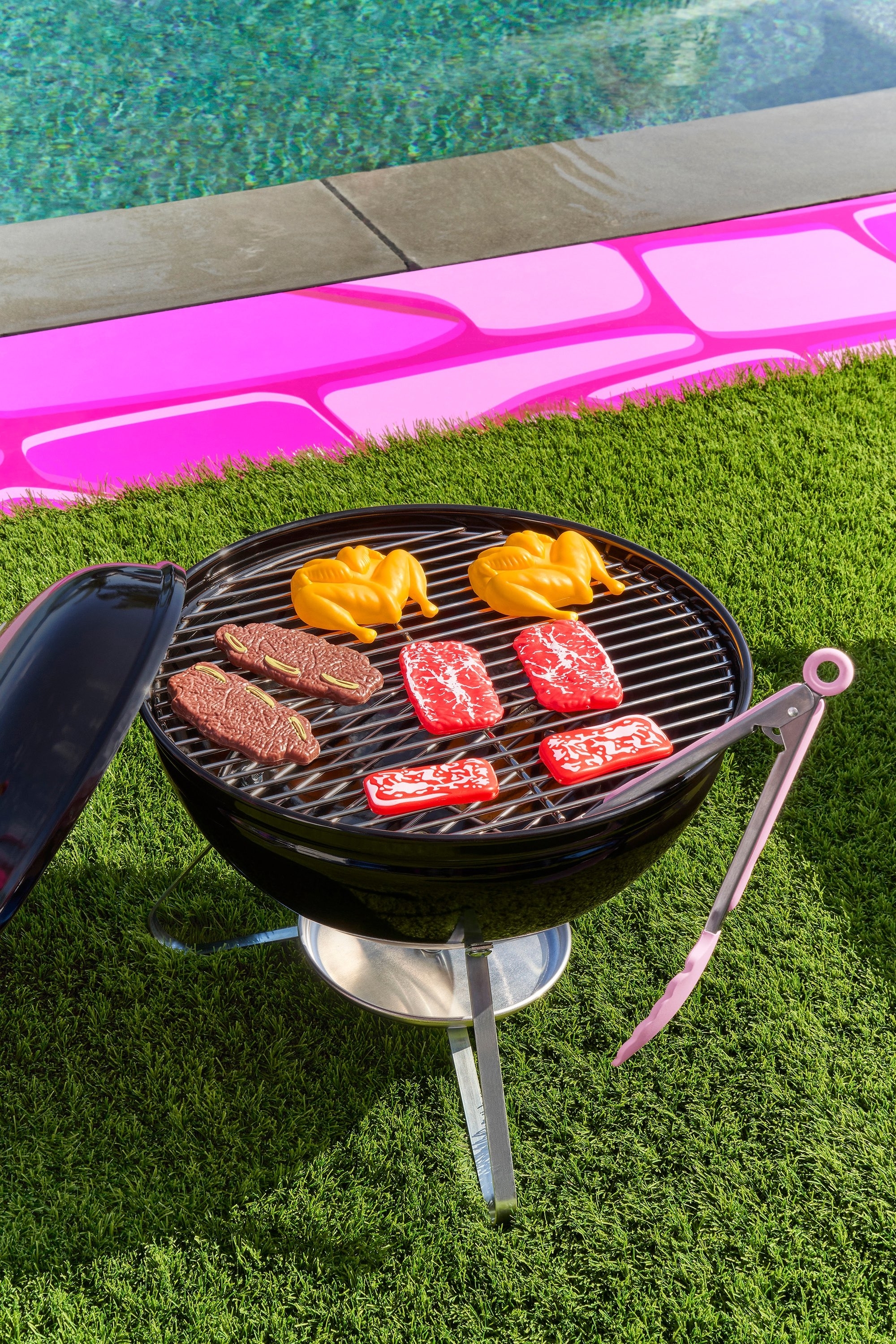 A fake grill featuring plastic chicken and beef and a pair of pink of plastic tongs