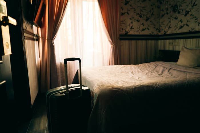 A dark hotel room with a luggage and empty bed