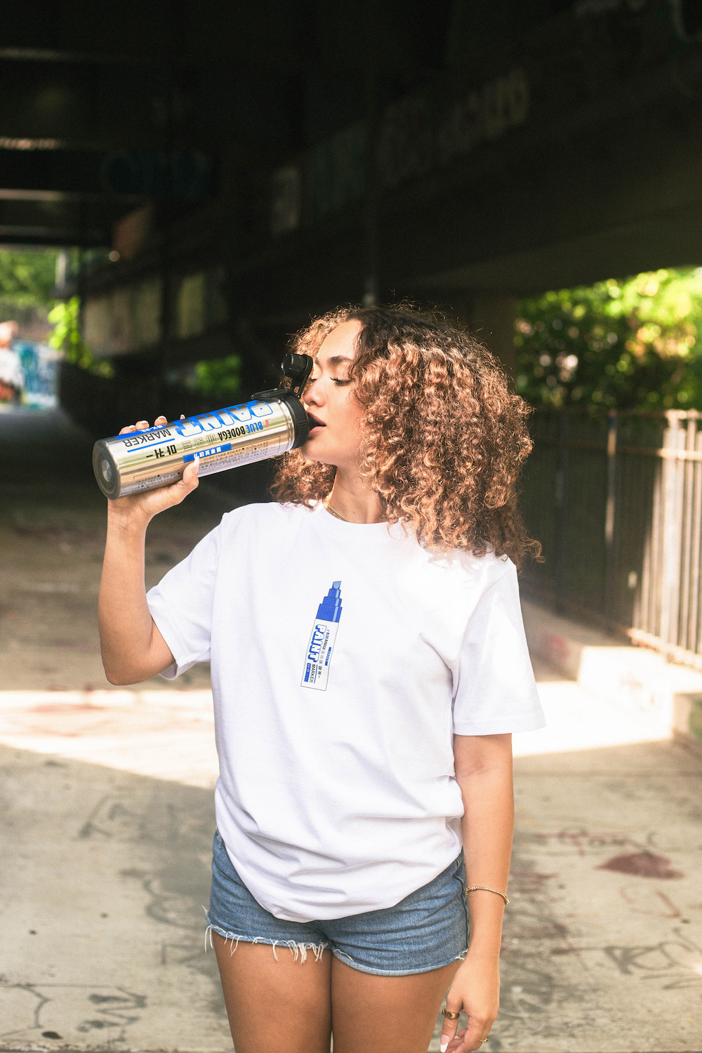 A model drinks from a Blue Bodega bottle that resembles a paint marker