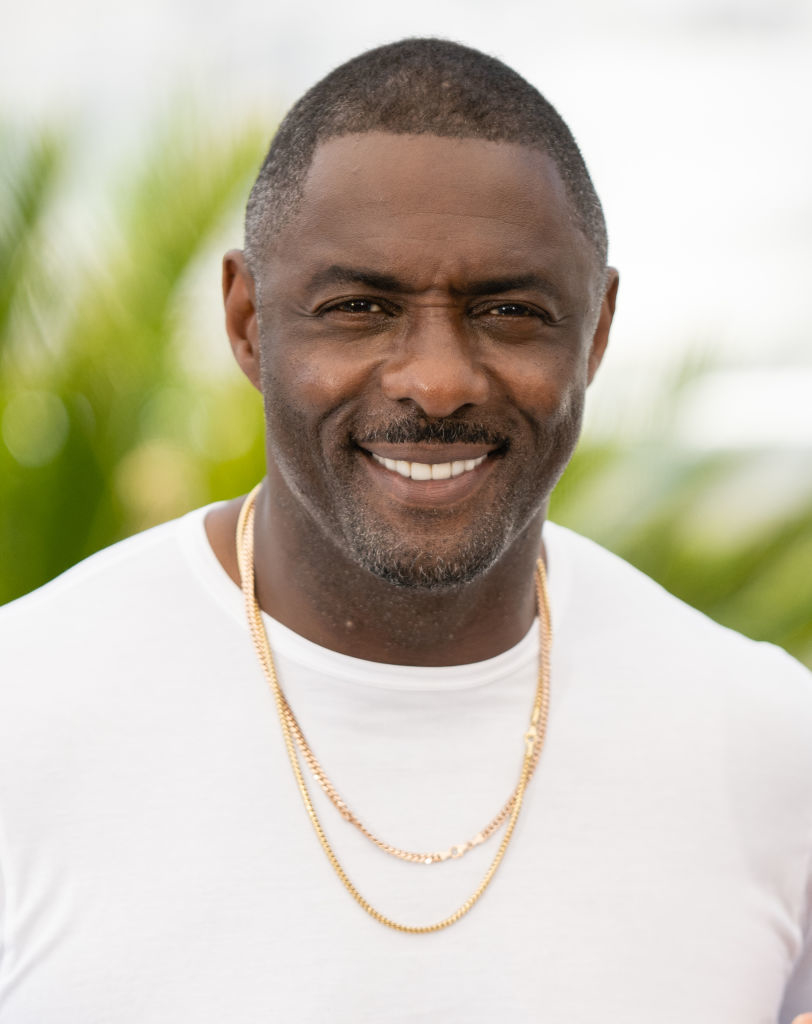 Close-up of Idris smiling and wearing two thin chain necklaces