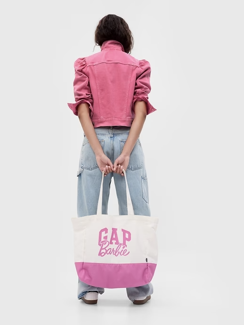 A model standing with their back to the camera while wearing the barbie gap jacket and holding the bag