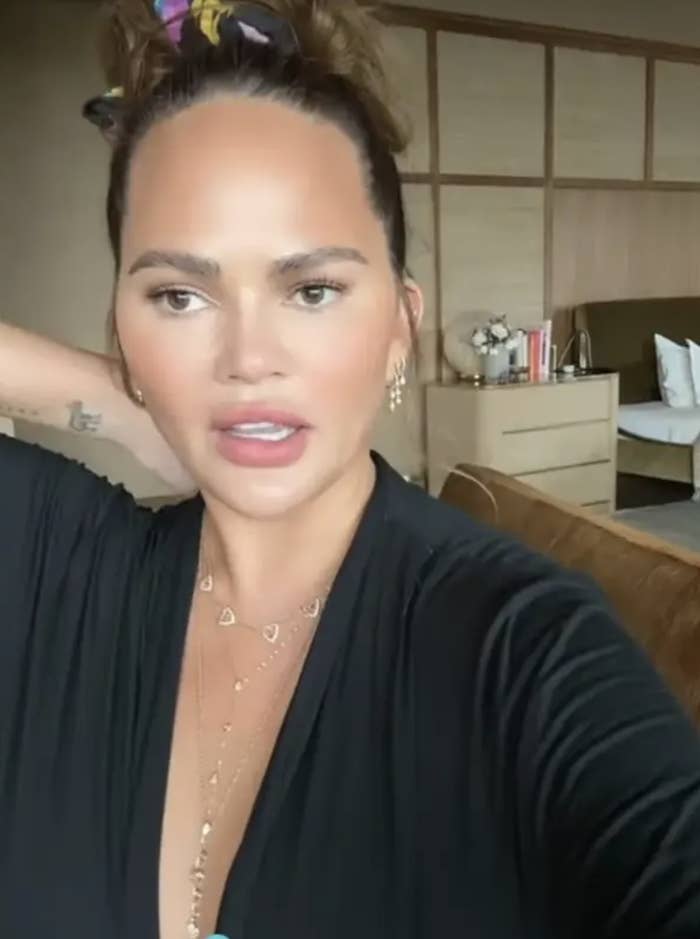 Chrissy Teigen speaking into her phone camera with her bedroom in the background
