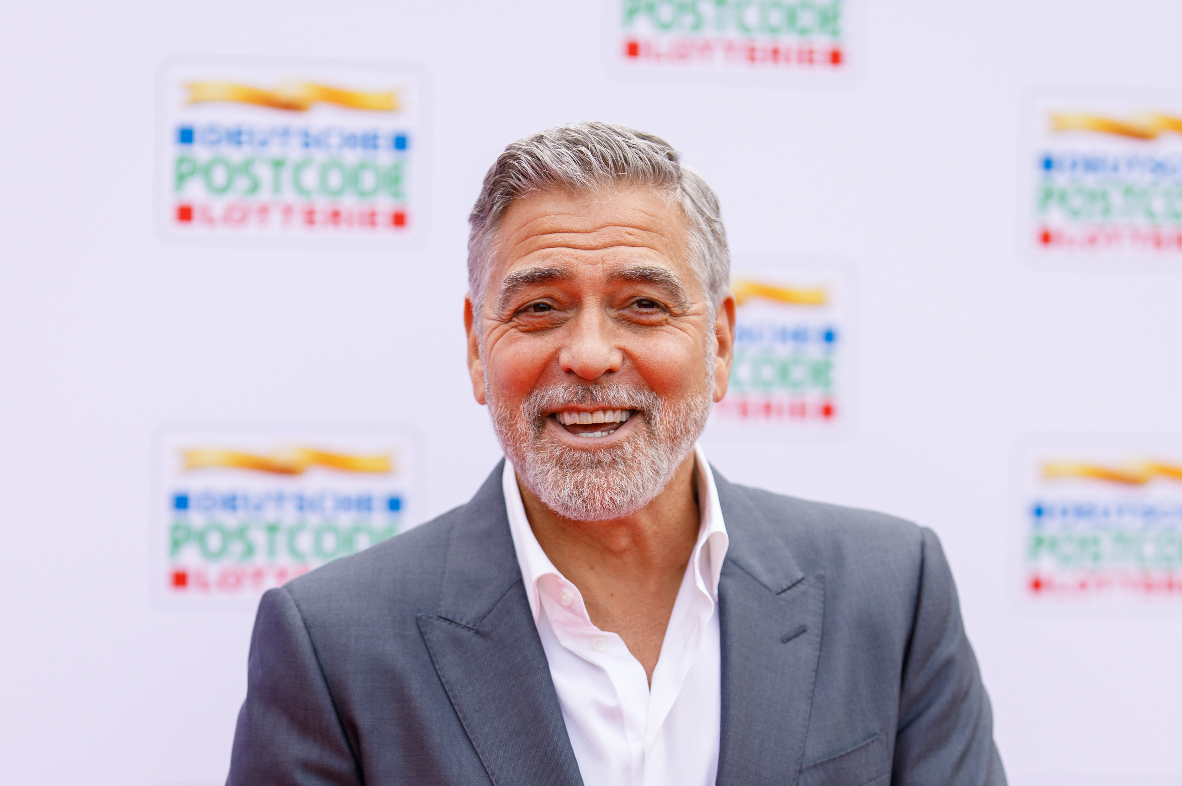 A red carpet shot of George Clooney wearing a grey suit and smiling