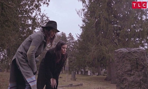 A screenshot of Steven and Liv Tyler standing in a graveyard, bending over and looking at a headstone