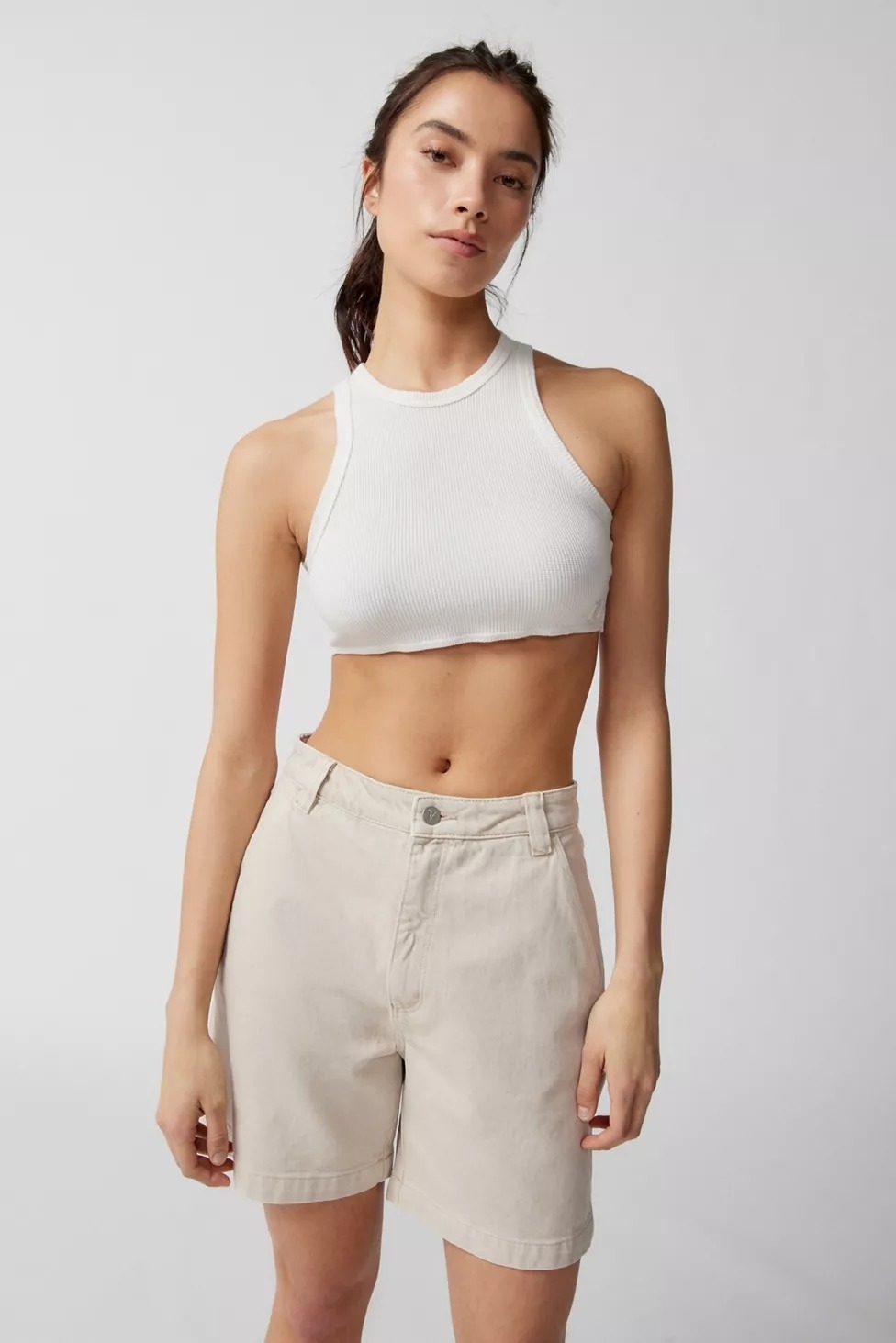Model wearing beige mid-thigh shorts with white crop top