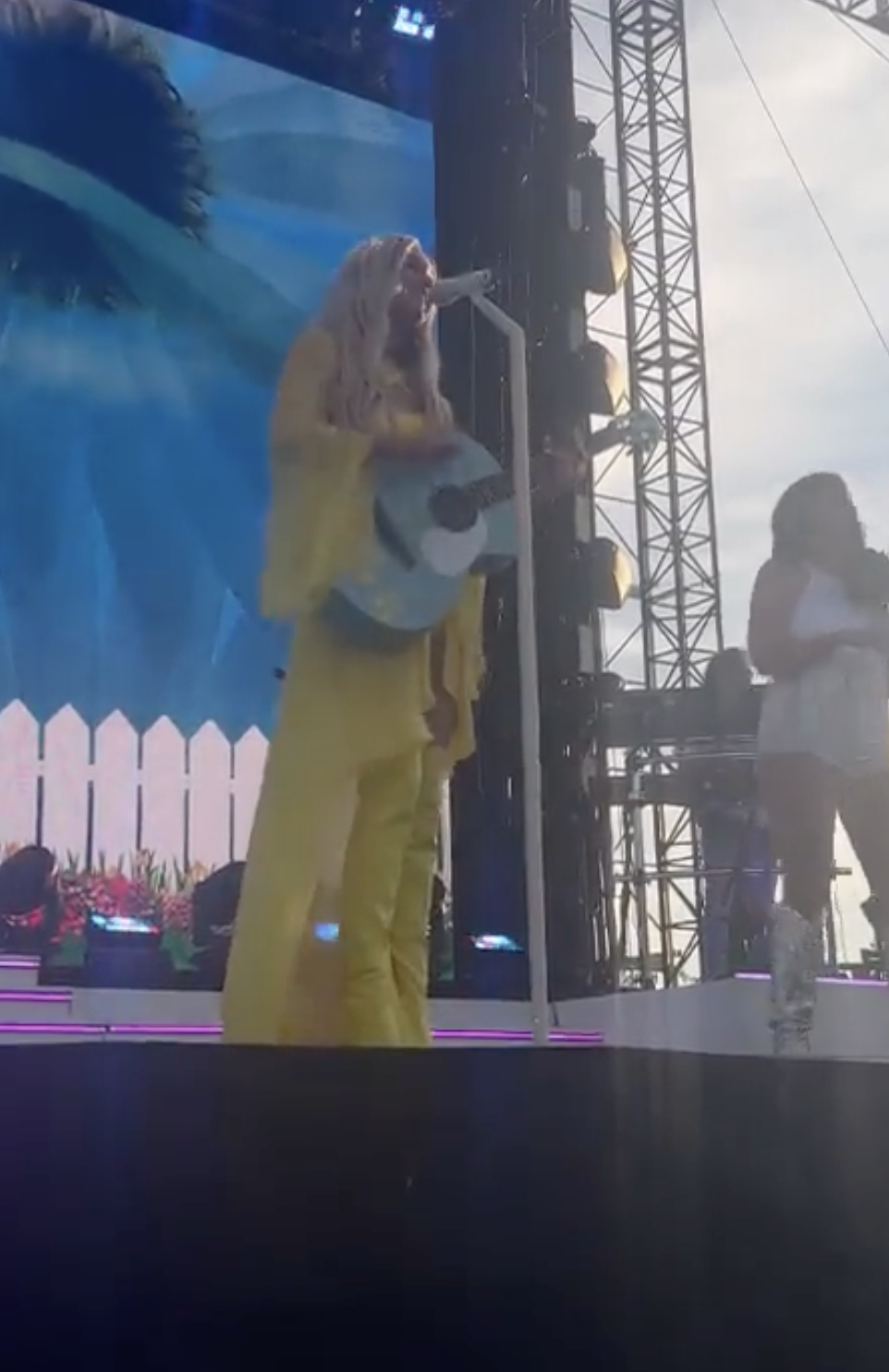 Kelsea Ballerini holding her guitar as she addresses from the stage