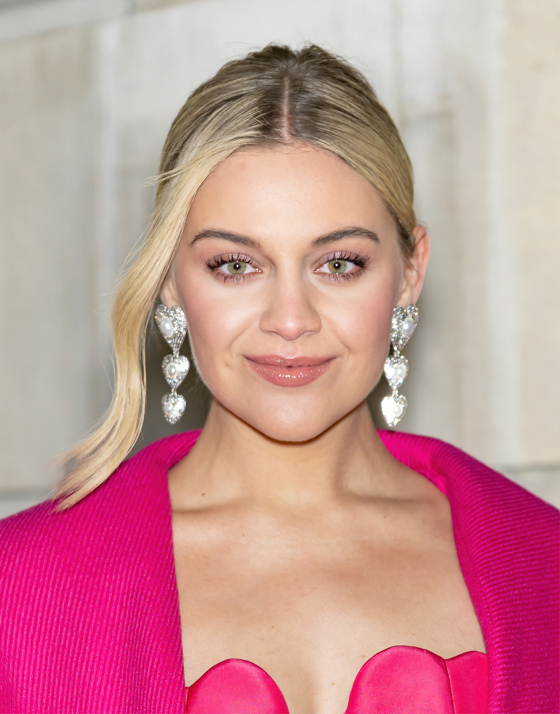 A closeup of Kelsea Ballerini, who&#x27;s wearing three-tiered heart-shaped earrings, smiling at the camera
