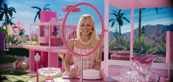 Margot Robbie as Barbie smiling an holding an over-sized brush