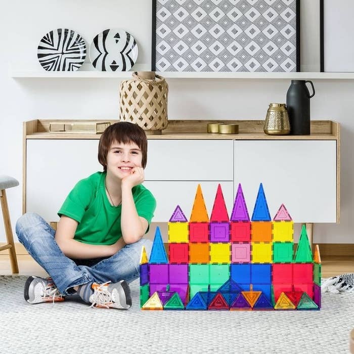 Child sits next to a magnetic tile castle
