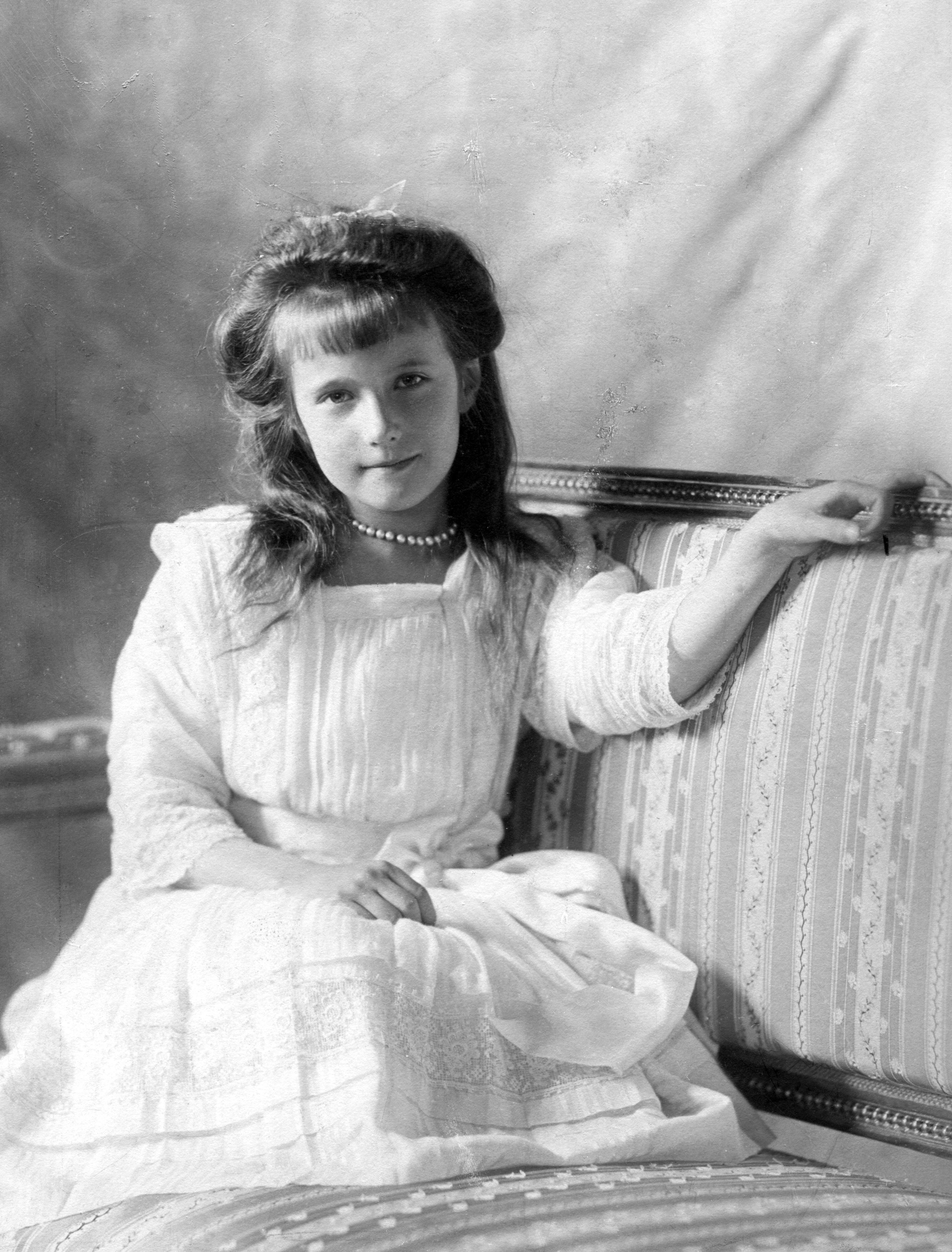 A Black and white photo of the real Anastasia as a child sitting on a couch while wearing a white dress,