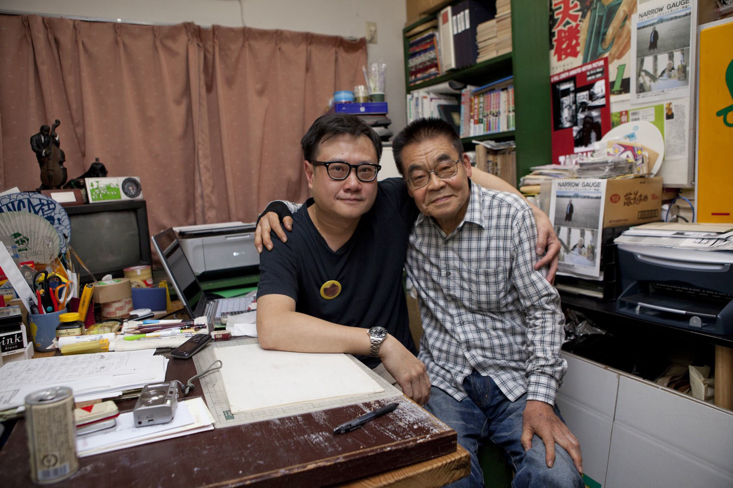 Photo of Yoshihiro Tatsumi sitting at his desk beside filmmaker Eric Khoo