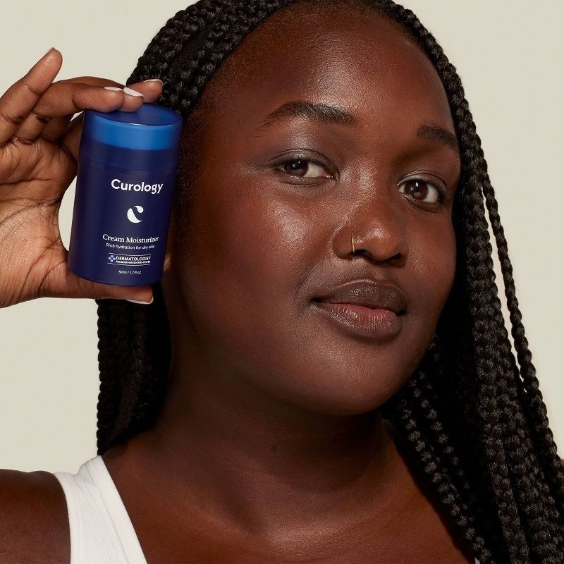 A person with braids holding a bottle of moisturizer