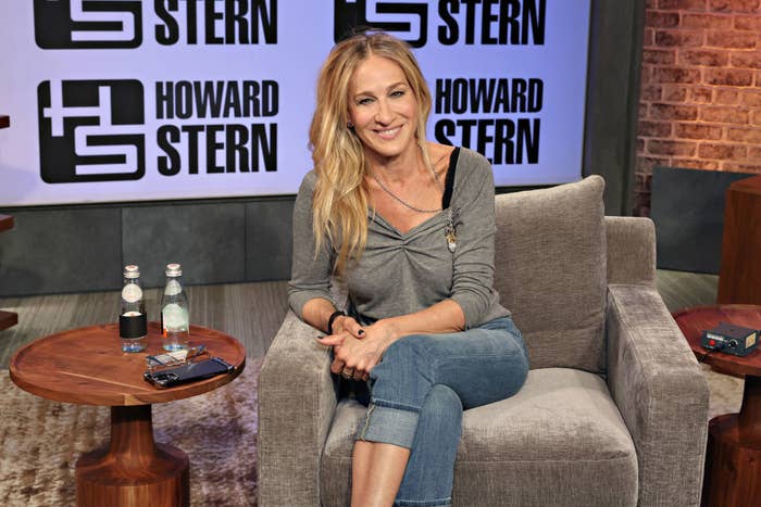 Close-up of SJP sitting in a chair and smiling  on the Howard Stern Show set