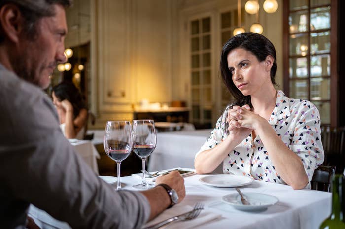 An unamused woman looking across at a man at a dining table