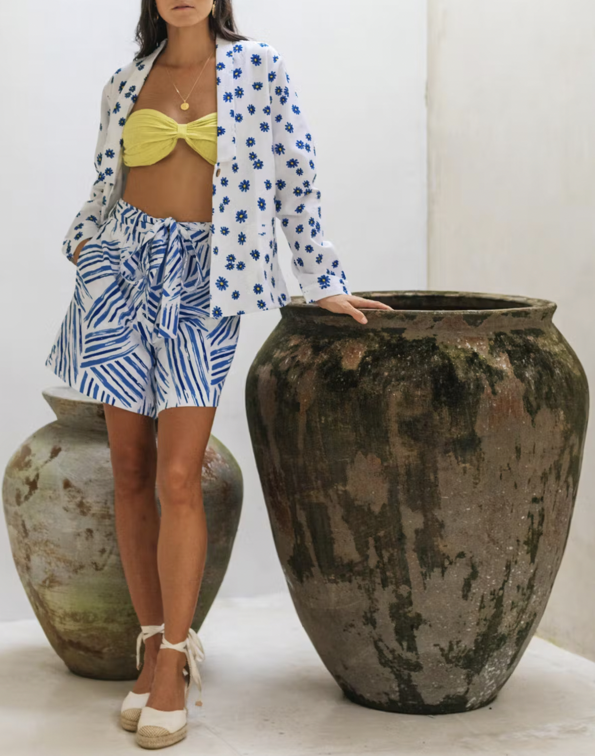 Model wearing blazer over bralette and standing with hand resting on pot