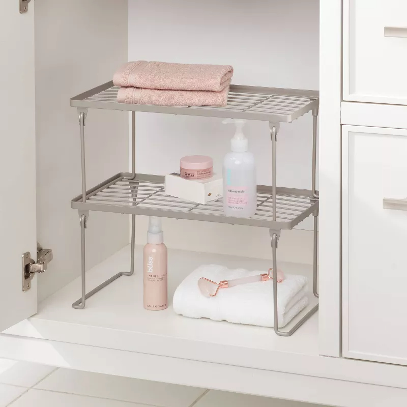 grey stackable wire shelf with shower supplies in a cabinet