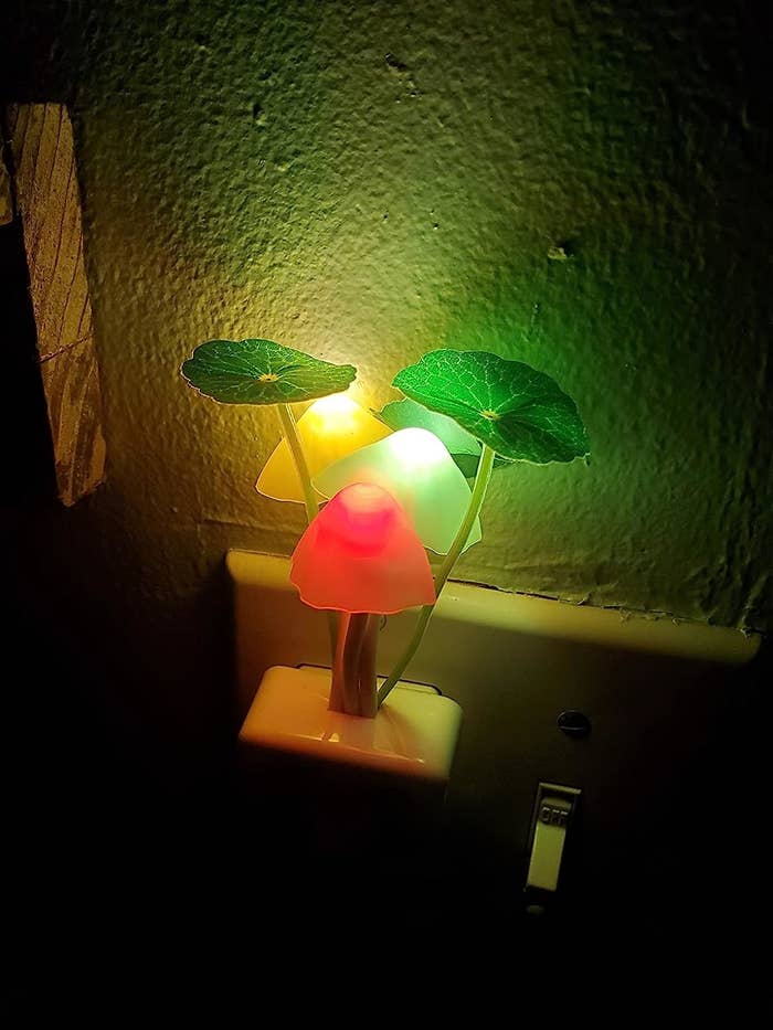 a reviewer photo of the multicolored night light plugged into a wall socket