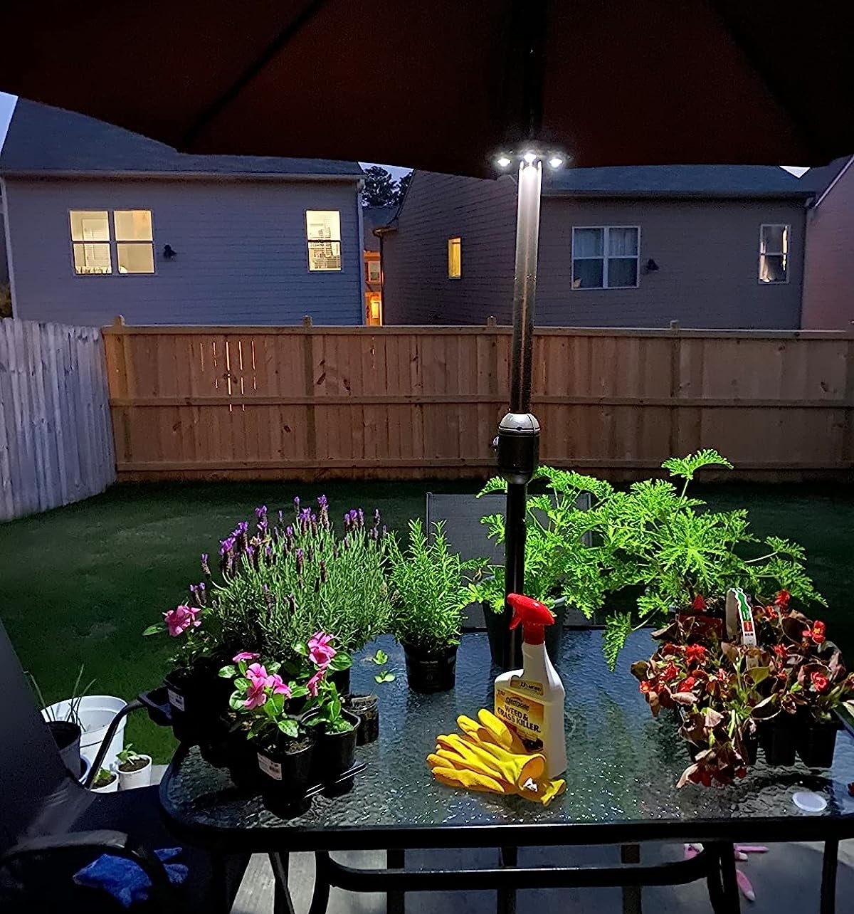 a reviewer photo of the light on the umbrella pole illuminating a table full of garden supplies in a dusky backyard