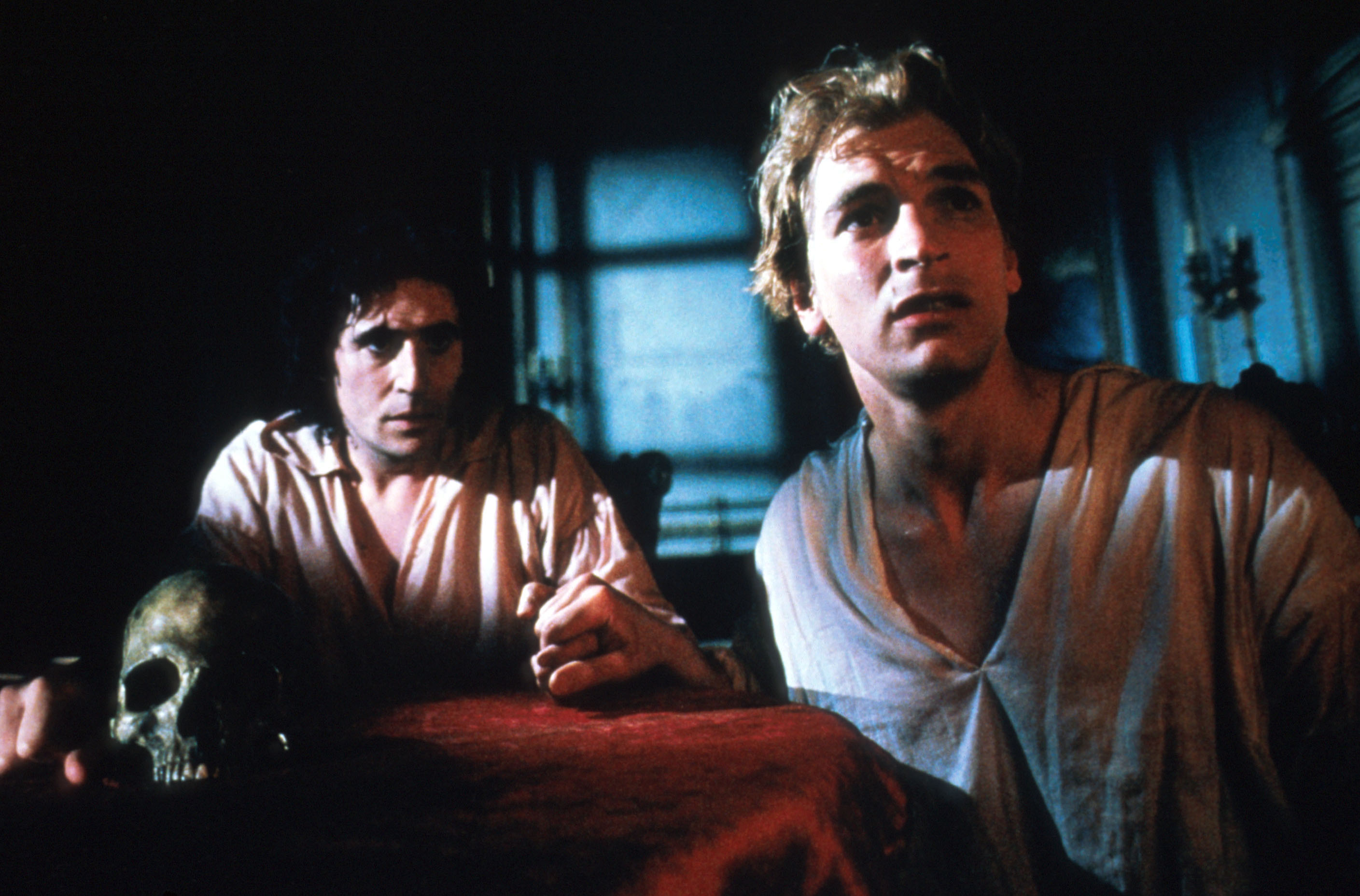 Julian Sands and Gabriel Byrne sit fearfully near a table adorning a skull