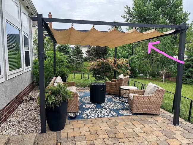 A reviewer's patio set with couch and two lounge chairs covered with the tan pergola