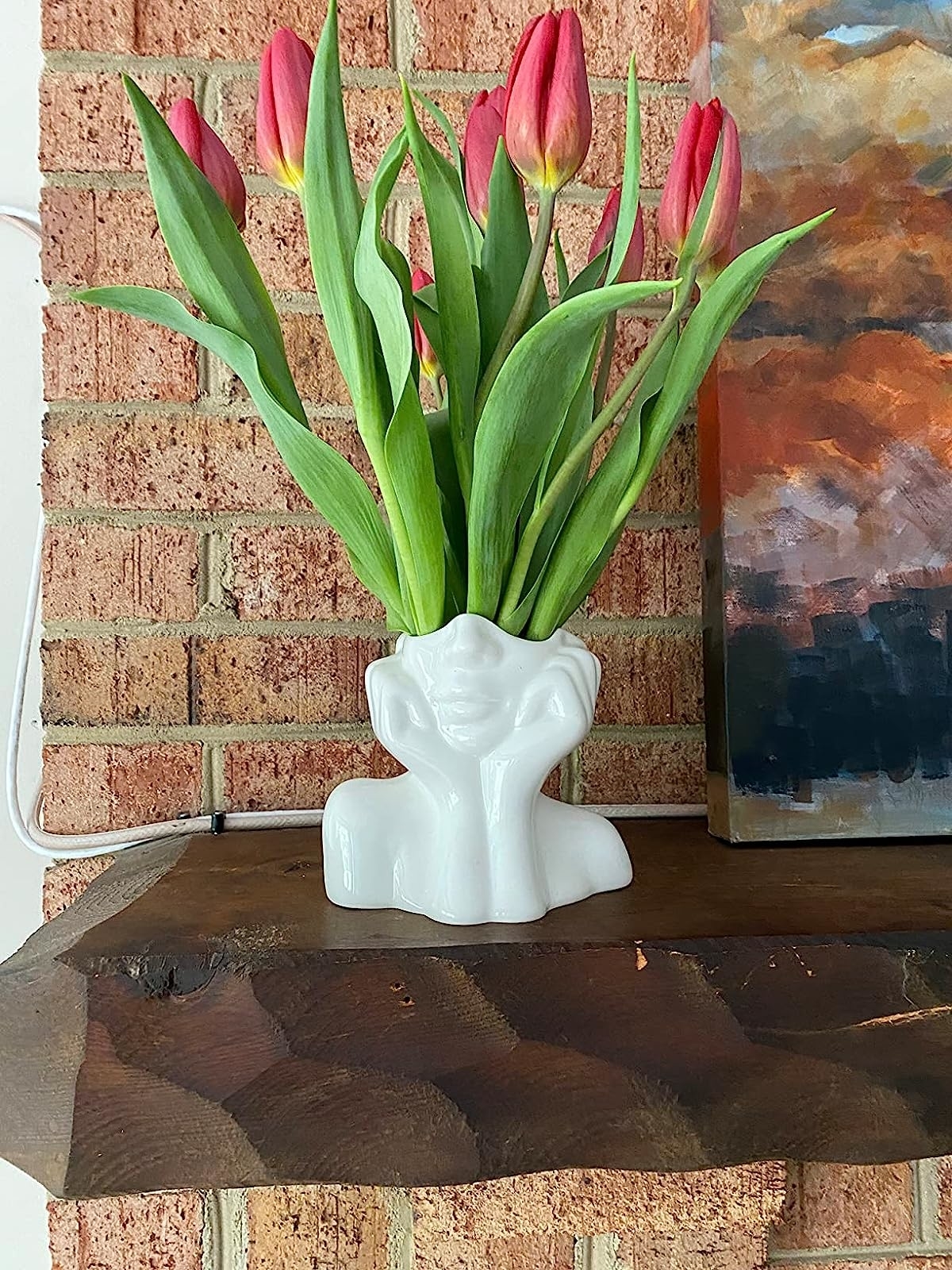 a reviewer photo of the white vase filled with tulips in front of a brick wall