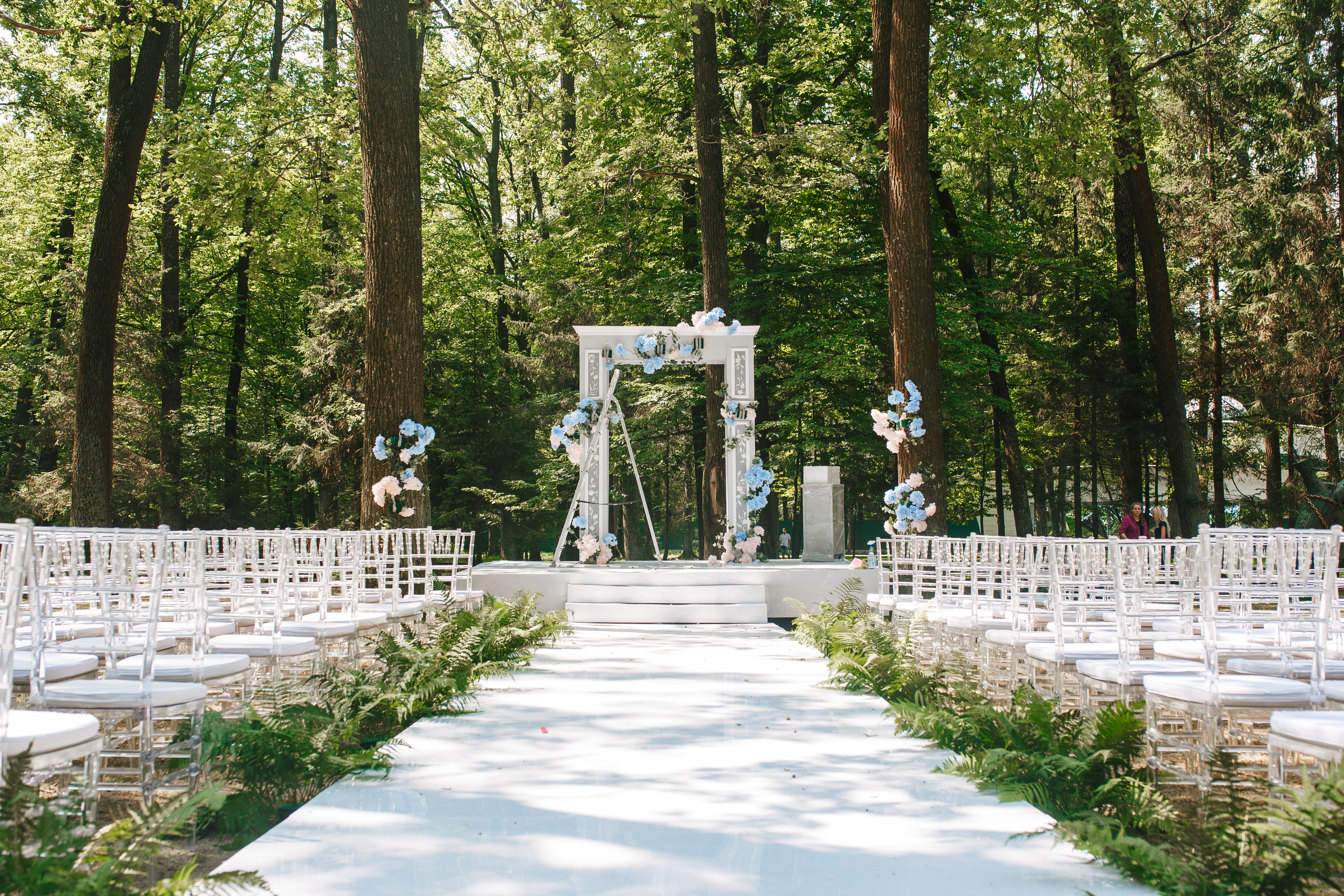 Empty wedding altar setup with white chairs and blue flowers with forest trees in the background