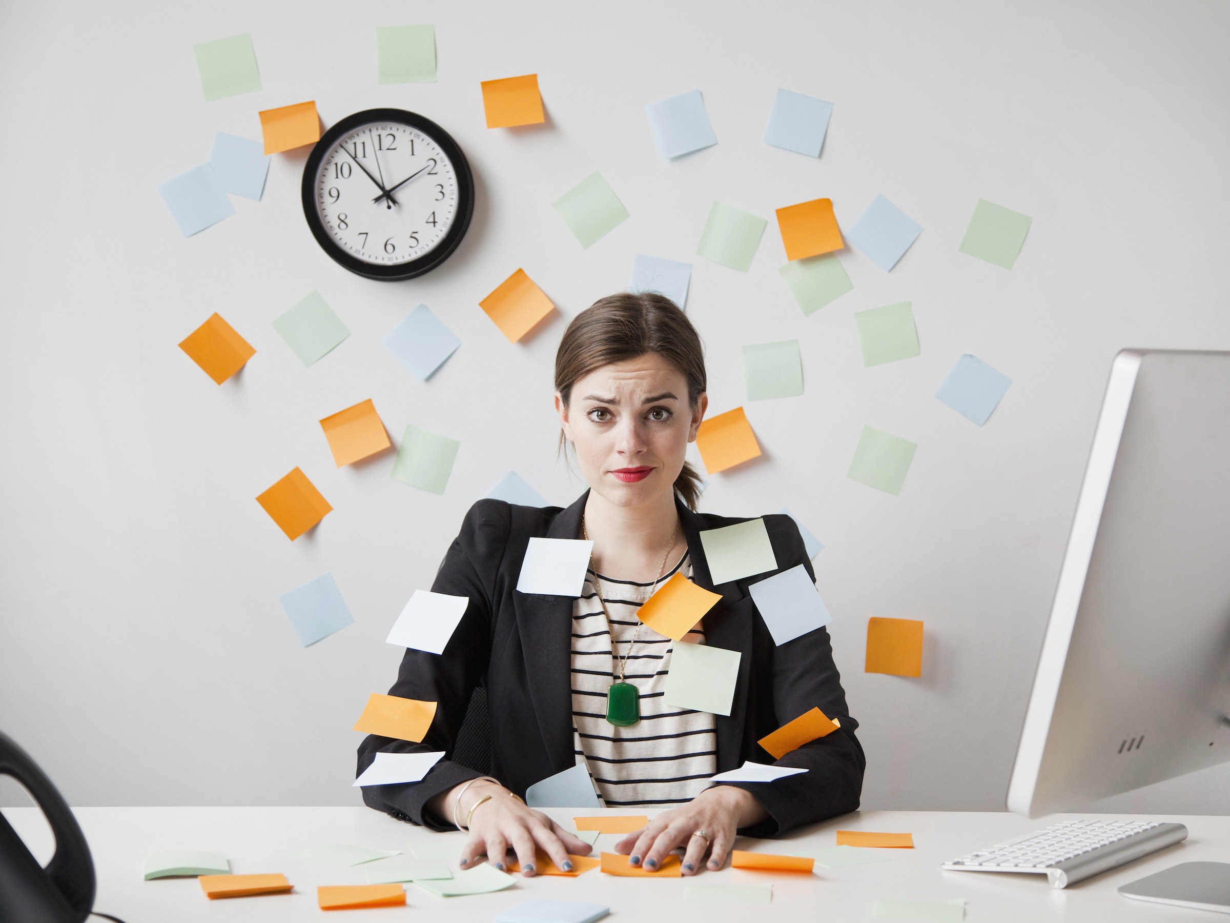 A woman at a desk with Post-its flying in the air and a clock behind her