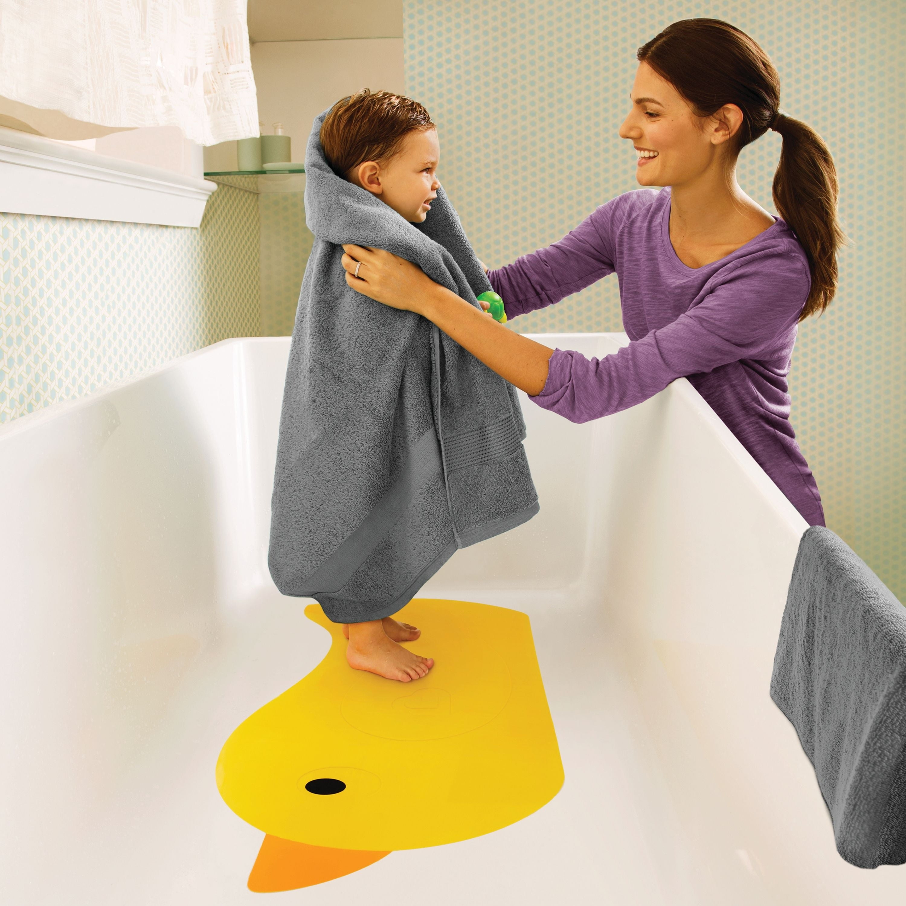 A child being wrapped in a towel by their parent while standing on the bath mat in the tub