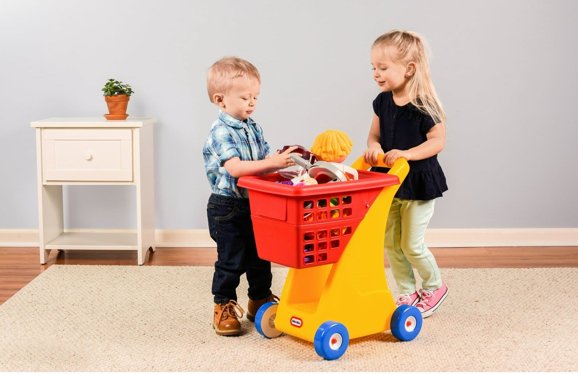 Two children putting toys into the pretend shopping cart.