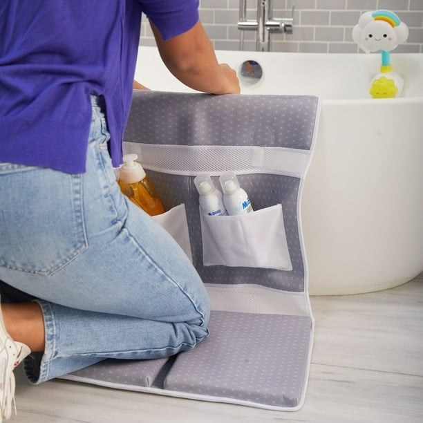 A person kneeling on the grey mat and reaching into the tub.