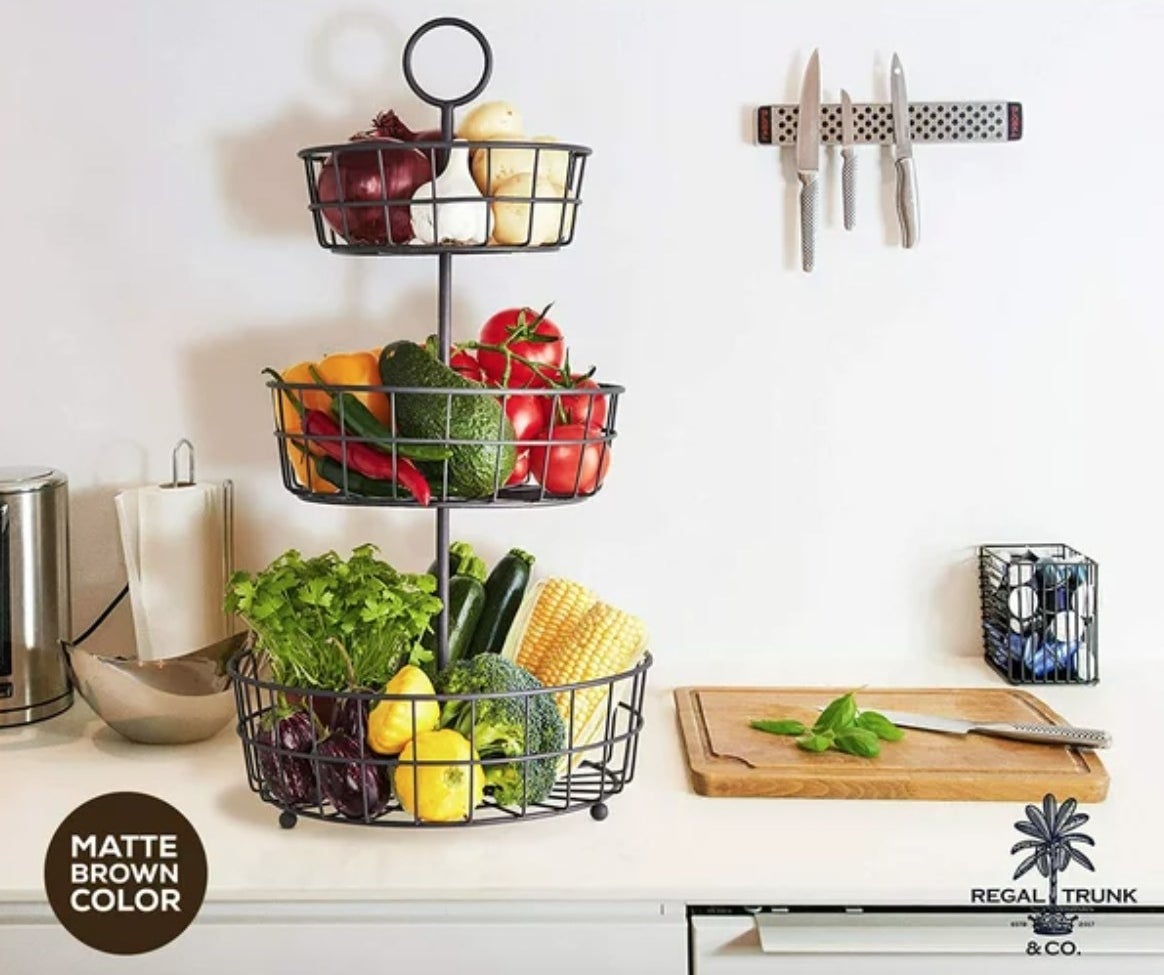 a tiered fruit basket filled with fruit and vegetables on a kitchen counter