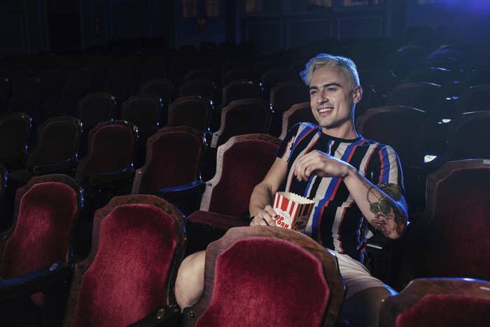 A young man in a movie theater eating popcorn and smiling