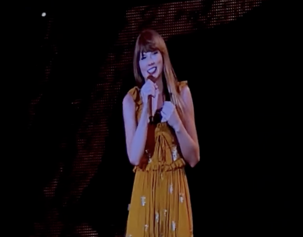 Taylor onstage smiling and holding a microphone