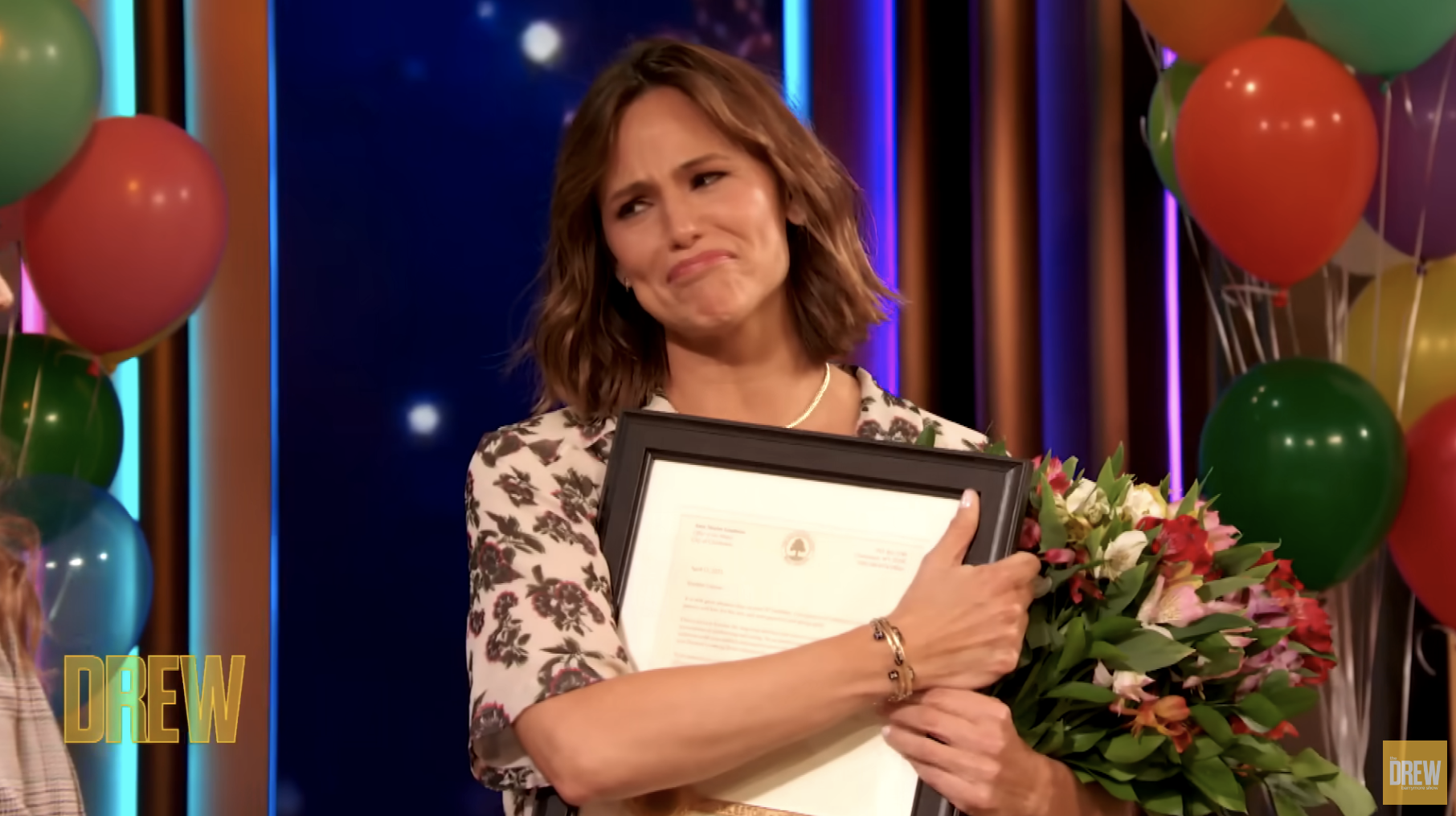 Closeup of Jennifer Garner holding a bouquet of flowers and a plaque from Drew
