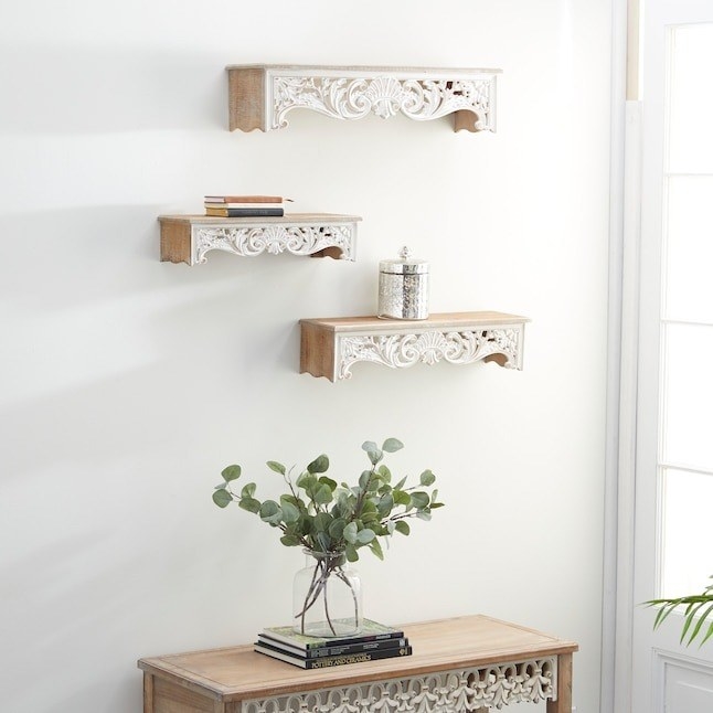 the trio of floating shelves with carvings on the bottom hanging on a wall