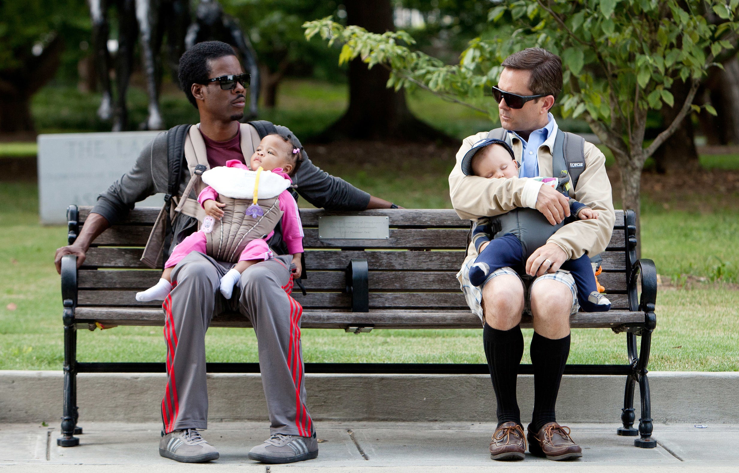 Two fathers sitting on a bench holding their kids