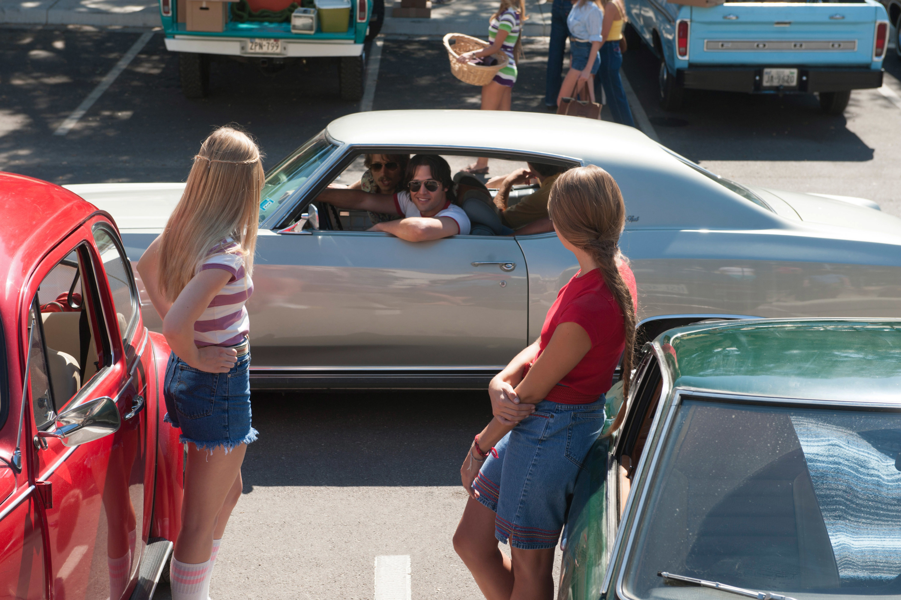 A car stopping to talk to two girls standing by their cars